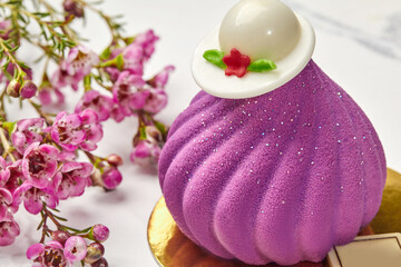 Violet swirl-shaped mousse pastry with chocolate hat and flowers