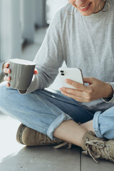 Smiling woman looking at smartphone screen while drinking morning coffee.