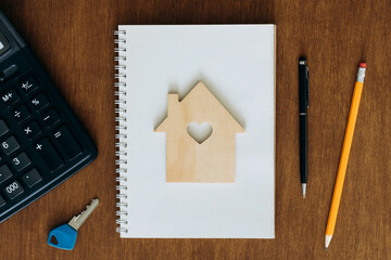 Blank notebook, calculator and model of a house on a wooden table, flat lay.