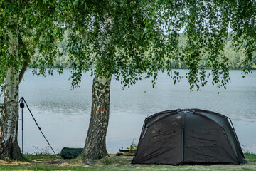 A serene camping setup by the lake with a tent and trees, creating a peaceful atmosphere blending...
