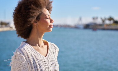 A woman with curly hair is standing on a pier overlooking a body of water