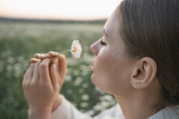 A woman is holding a flower and smelling it. Concept of peace and tranquility, as the woman is enjoying the simple pleasure of smelling a flower in a field. The scene is serene and calming