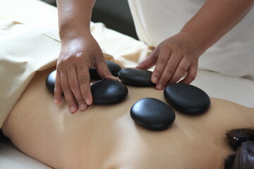 Close-up cut of professional masseuse doing hot stone massage service to her female customer, relaxation, spa treatment, wellness, resort, hotel, leisure.