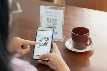 Detail of customer hand making payment through smartphone and scan code at cafe.
