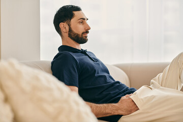 A man with a beard sits comfortably on a couch in a modern living room, enjoying quality time