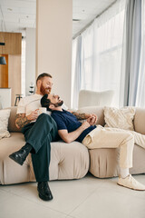 Fototapeta premium Two men, a happy gay couple, dressed casually, sit together on a modern living room couch, enjoying each others company.