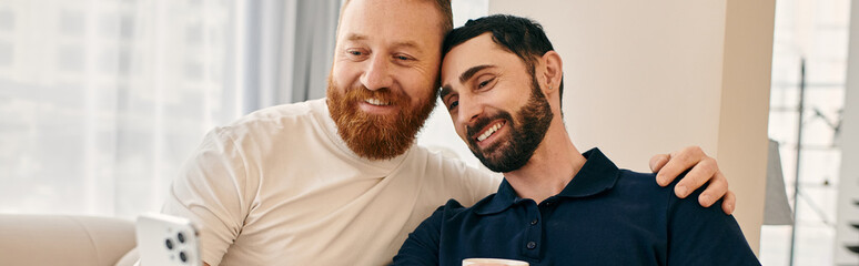 Happy gay couple in casual clothes, with beards, share a warm embrace on a comfortable couch in a...