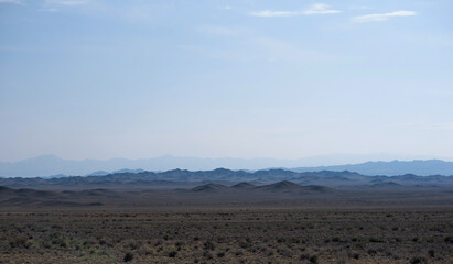 a vast desert landscape under a clear sky with layered mountain silhouettes receding into the distance, creating a serene and expansive view