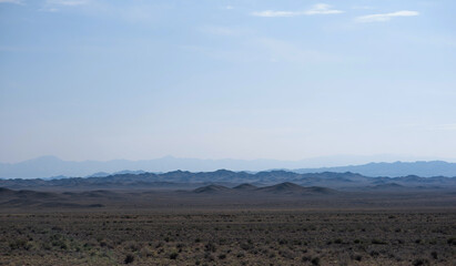 a vast desert landscape under a clear sky with layered mountain silhouettes receding into the...