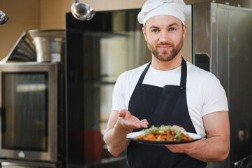 Food concept. One young chef dressed in uniform holding in his hands ready dish in restaurant