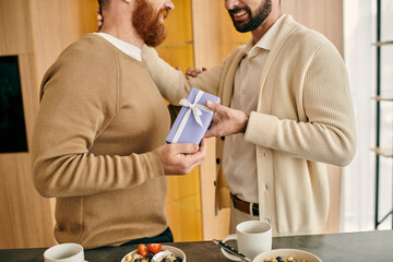 Two men joyfully exchange gift in a modern kitchen, showcasing love and friendship in an intimate...