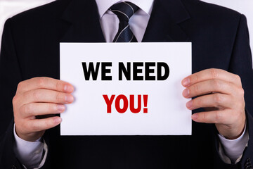 Obraz premium Businessman holding a card with text we need you