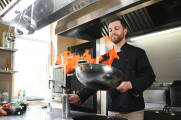 Chef in restaurant kitchen at stove and pan cooking flambe on food