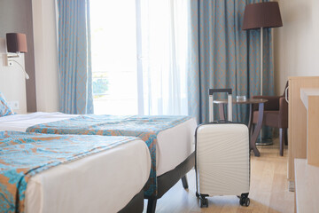 Comfortable bedroom with two beds, white suitcase in hotel during travelling.