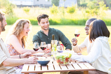 A diverse group of friends laughing and enjoying wine outdoors, creating a joyful and relaxed...
