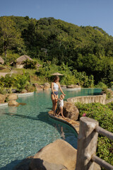 Mother and baby play in outdoor infinity swimming pool of luxury hotel resort in tropics. Happy...