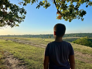 Young traveler on the hill, happy man takes a deep breath of fresh air in nature, breathing clean air. Guy enjoying nature