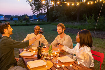 A group of friends enjoying an evening outdoor dinner, raising glasses to toast under charming...