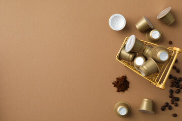 Golden coffee capsules in shopping tray, coffee beans on beige background, space for text