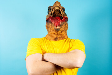 Person in dinosaur mask standing with crossed arms on blue background