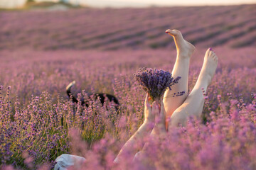 A woman is laying in a field of purple flowers with her legs spread out. She is holding a bouquet of flowers in her hands. The scene is peaceful and serene.