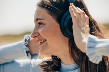 A joyful woman smiling and enjoying music with headphones outdoors on a sunny day in a serene and...