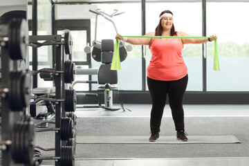 Fototapeta premium Corpulent woman standing on a mat and exercising with a rubber band