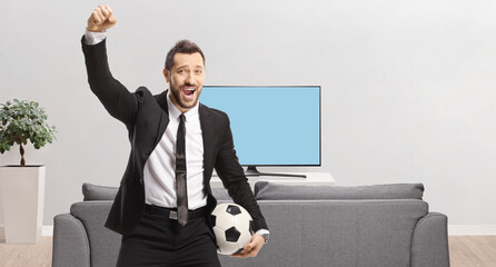 Businessman holding a soccer ball and cheering in front of a sofa