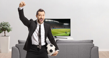 Businessman holding a soccer ball and cheering, watching a football match on tv