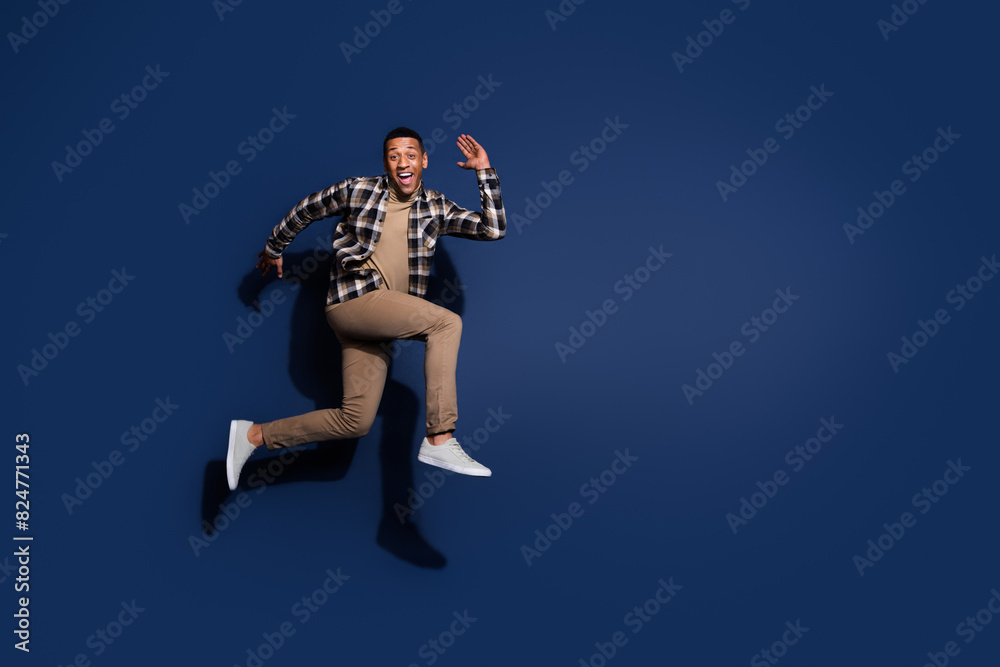 Poster Full length photo of handsome good mood guy wear checkered shirt jumping high running emtpy space isolated blue color background