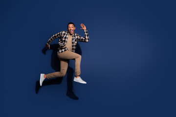 Fototapeta premium Full length photo of handsome good mood guy wear checkered shirt jumping high running emtpy space isolated blue color background
