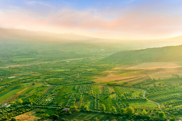 scenic rustic landscape with green hills and farms in a mountain valley during colorful cloudy sunset