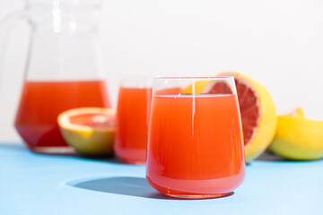 Grapefruit juice in a glass among fresh grapefruits on blue and white background