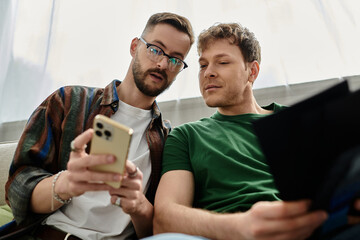 Two men in love sit on a couch, focused on a cell phone screen.