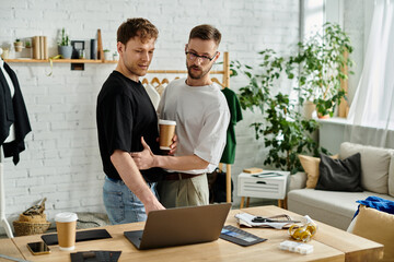 Two men, a gay couple, stand in atelier, engrossed in their laptop screen.