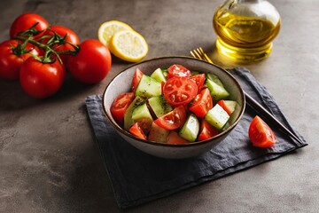 Tomato and cucumber salad with olive oil and lemon juice in a bowl on a dark background. Sprig of...