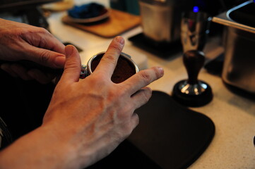 Close up of male barista making coffee while holding tamper in the hand, going to press ground coffee in holder. Coffee preparation service concept