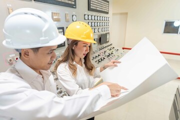 Amid the challenges of the industrial landscape Two male and female Asian engineers at a power plant demonstrate their resiliency. Using a blueprint to overcome obstacles and drive progress.