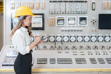 Asian female engineer working in power plant with laptop at steam engine control board symbolizing...