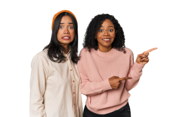 Young Latin friends together in studio shocked pointing with index fingers to a copy space.