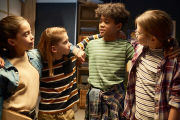 Four cute intercultural kids in casualwear looking at each other during chat while standing in embrace in front of camera at home