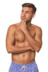 Fototapeta premium Young man shirtless in swimwear, studio looking sideways with doubtful and skeptical expression.