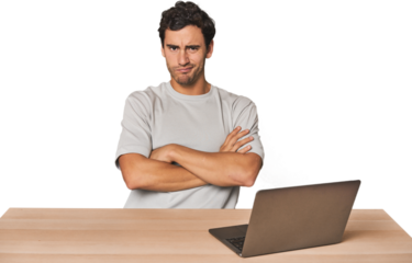 Hispanic young man working on laptop frowning face in displeasure, keeps arms folded.