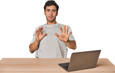 Hispanic young man working on laptop being shocked due to an imminent danger