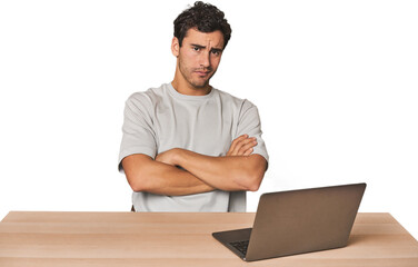 Hispanic young man working on laptop suspicious, uncertain, examining you.