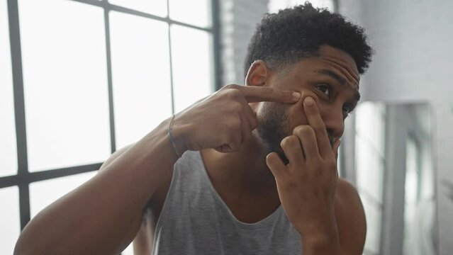 African american man squeezing pimple in bright home interior