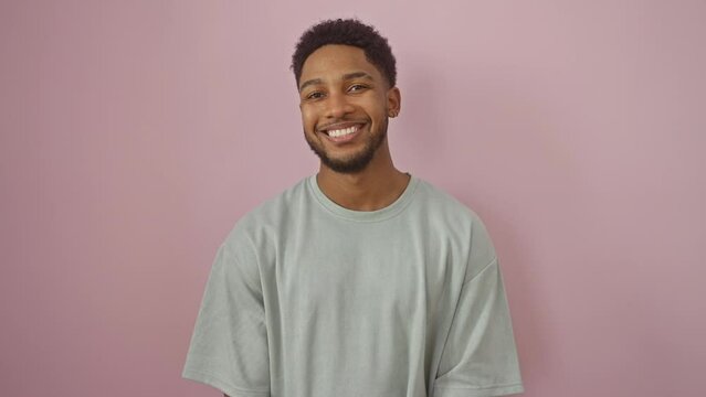 Hilarious african american man sticking tongue out while standing, wearing a t-shirt against isolated pink background. happy guy flaunting a fun, amusing expression.