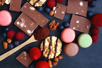 Macarons, chocolate, cookies, berries and various nuts on dark blue background. Top view.