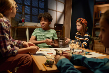 African American boy in t-shirt looking at one of his friends during board game and shaking dice in hands before throwing it