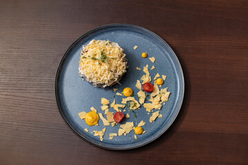 A blue plate with a dish of food on it. The plate is topped with a yellow sauce and some shredded cheese